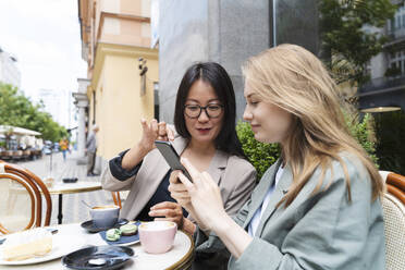 Businesswoman showing over smart phone to partner at sidewalk cafe - NDEF00852