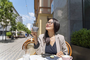 Smiling businesswoman enjoying coffee at sidewalk cafe - NDEF00856