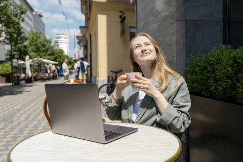 Businesswoman enjoying coffee with laptop on table at sidewalk cafe - NDEF00859