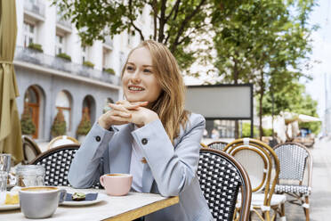Lächelnde Geschäftsfrau, die in einem Straßencafé sitzt - NDEF00863