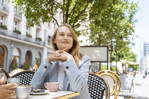Nachdenkliche Geschäftsfrau, die in einem Straßencafé sitzt - NDEF00864