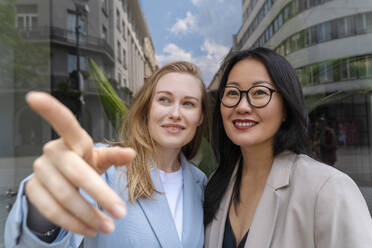 Businesswoman pointing by colleague in front of glass wall - NDEF00875