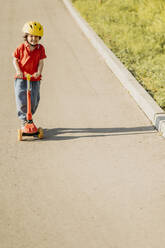 Lächelnder Junge, der auf dem Fußweg einen Motorroller fährt - ANAF01572