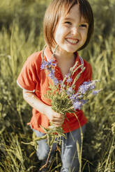 Lächelnder Junge hält einen Blumenstrauß auf einem Feld - ANAF01573