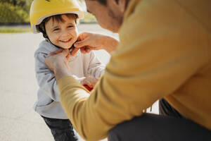 Father tying helmet on smiling son - ANAF01574