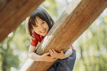 Lächelnder Junge spielt auf einem Holzstamm - ANAF01577