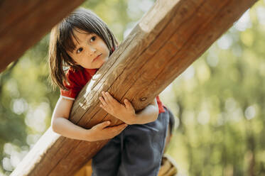 Boy hanging on wooden log in park - ANAF01578