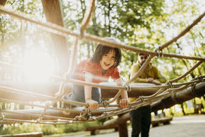 Lächelnder Junge spielt an einem Seil im Klettergerüst - ANAF01580
