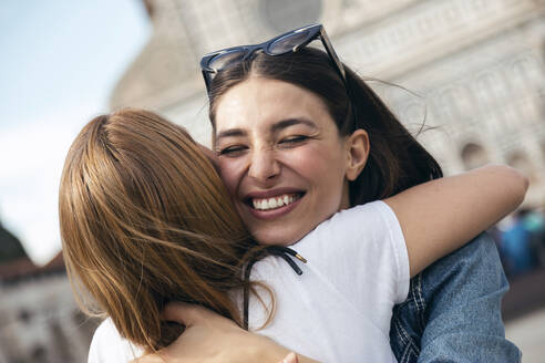 Smiling woman embracing friend in city - JSRF02548