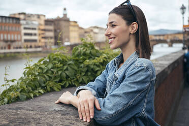 Contemplative woman looking at river leaning on wall - JSRF02556