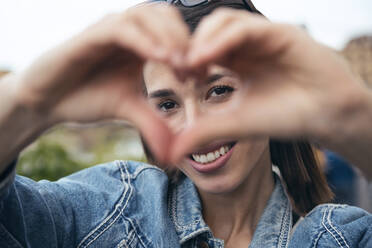 Smiling woman making heart shape - JSRF02557