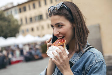 Lächelnde Frau isst Pizza und spricht mit ihrem Smartphone - JSRF02564