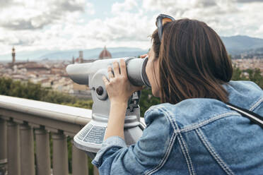 Woman looking through binoculars standing at balustrade - JSRF02567
