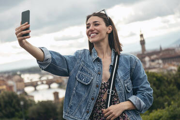 Eine fröhliche Frau hält einen Moment in der Stadt mit einem Selfie fest - JSRF02568