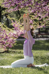 Teenager-Mädchen mit erhobenen Armen übt Yoga in einem blühenden Park - AAZF00743