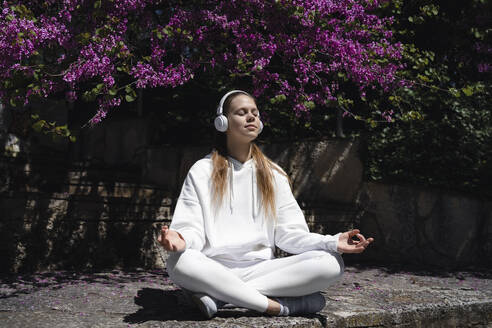 Teenager-Mädchen hört Musik mit Kopfhörern und meditiert an einer Mauer im Park - AAZF00744