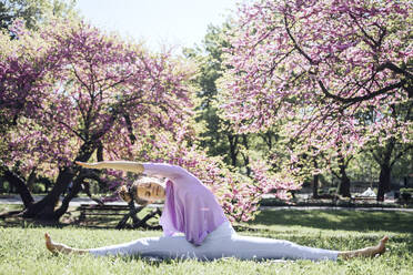 Teenager-Mädchen mit gespreizten Beinen übt Yoga im Park in der Blüte - AAZF00746