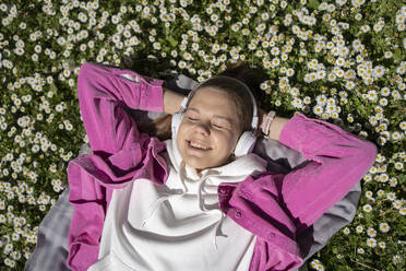 Teenager-Mädchen hört Musik mit Kopfhörern, die auf einem Blumenbeet im Park liegen - AAZF00752