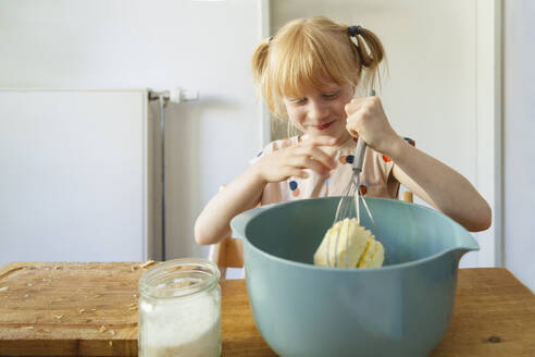 Lächelndes Mädchen bei der Herstellung von Kuchenteig mit einem Handrührgerät zu Hause - IHF01400