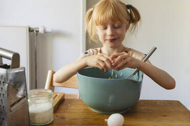 Smiling girl breaking egg into bowl at home - IHF01403