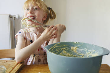 Glückliches Mädchen, das zu Hause Kuchenteig mit dem Schneebesen probiert - IHF01405