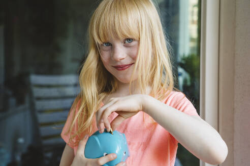 Lächelndes Mädchen spart eine Münze im Sparschwein - IHF01406