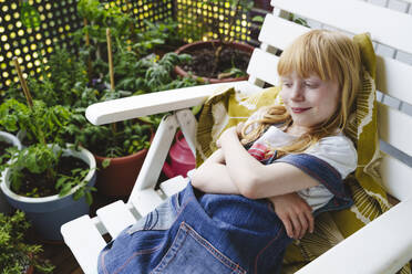 Lächelndes Mädchen, das sich auf einem Sessel auf dem Balkon ausruht - IHF01413