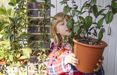 Lächelndes Mädchen mit Topfpflanze auf dem Balkon - IHF01415