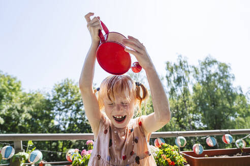 Fröhliches Mädchen, das sich auf einem Balkon Wasser auf den Kopf gießt - IHF01421