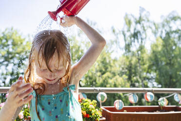 Blondes Mädchen gießt Wasser auf den Kopf auf dem Balkon - IHF01423