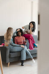 Freunde sitzen auf dem Sofa und tragen Lidschatten auf eine Frau auf - EHAF00042