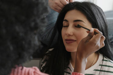 Friend applying makeup on woman and another friend braiding hair - EHAF00044