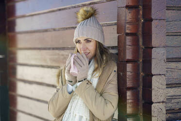 Contemplative woman drinking coffee near cottage in winter - JSMF02773