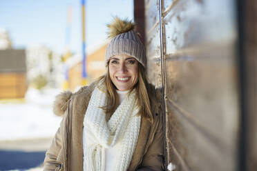 Smiling woman standing next to cottage in winter - JSMF02779