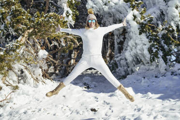 Lächelnde Frau mit Sonnenbrille beim Springen im Schnee - JSMF02782