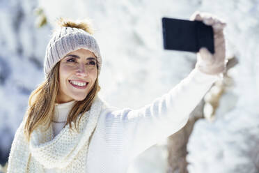 Eine fröhliche Frau mit Mütze hält mit einem Selfie einen Moment der Freude inmitten des Winterschnees fest - JSMF02794