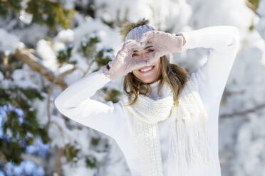 Smiling woman making heart sign in winter landscape - JSMF02795