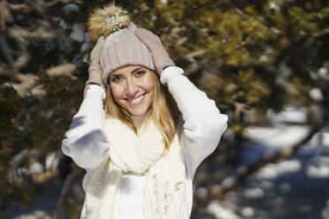 Smiling woman adjusting cap in winter - JSMF02801