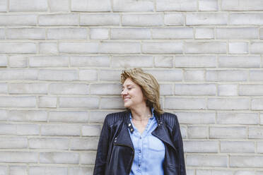 Smiling woman with eyes closed standing in front of brick wall - IHF01446