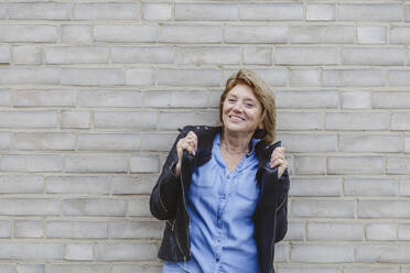 Senior woman standing in front of brick wall - IHF01447