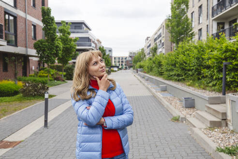 Contemplative woman standing near residential area - IHF01458