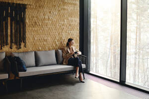 Thoughtful businesswoman enjoying coffee sitting in lobby at convention center - DSHF00842