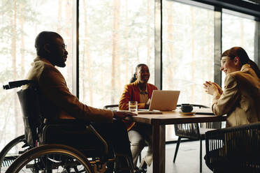 Geschäftsmann im Rollstuhl diskutiert mit Kollegen am Konferenztisch im Kongresszentrum - DSHF00855