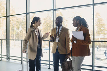 Businesswoman discussing with colleagues by glass window in convention center - DSHF00871