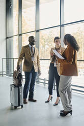 Businessman holding suitcase discussing with colleagues by glass window in convention center - DSHF00873