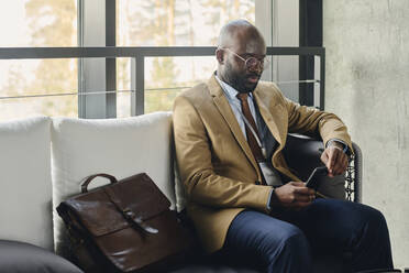 Businessman using smart phone sitting on sofa in lobby at convention center - DSHF00883