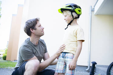 Lächelnder Vater mit Sohn, der einen Helm trägt, vor einem Gebäude stehend - NJAF00428