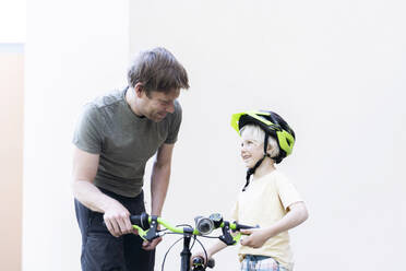 Glücklicher Vater und Sohn stehen mit Fahrrad vor einer Mauer - NJAF00429