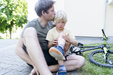 Father kissing and caring son fallen down from bicycle at footpath - NJAF00433