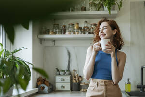 Lächelnde junge Frau steht mit Kaffeetasse zu Hause - OSF01780